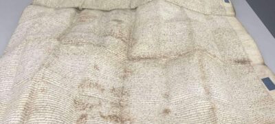 A sheet of parchment lies open on a table. It does not lie flat.