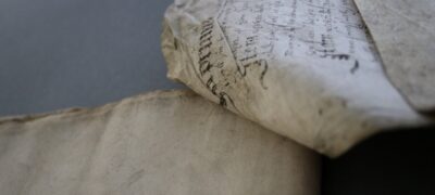 A close up of sheets of parchment which are sewn at their corners. One page is turned and lifting, while the other is flat.
