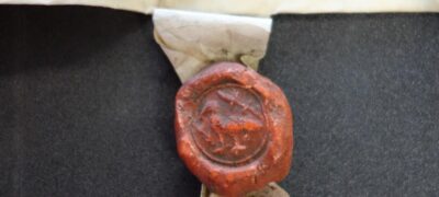 A red wax pendant seal attached to a parchment document is sitting on a black flat pad.