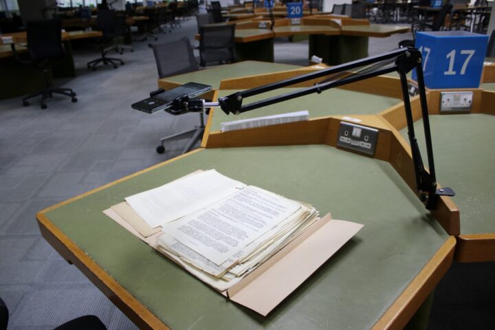 A tagged file is open on a table. Above it, a camera stand is holding a phone, ready to take a photo of the open page.