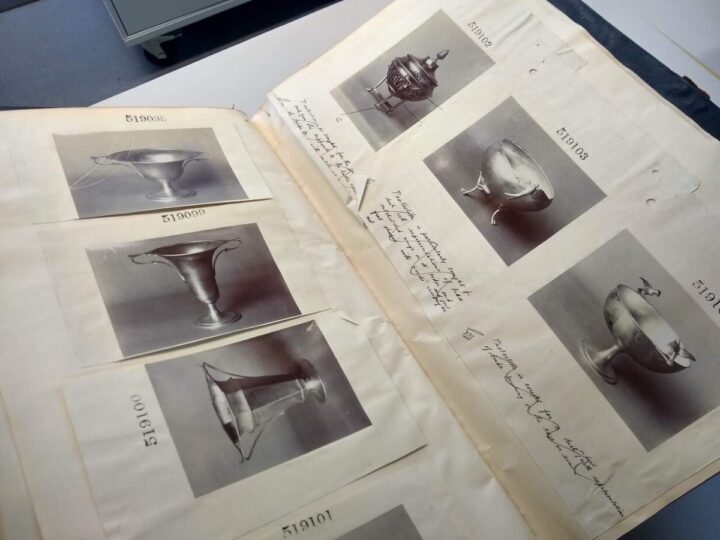 An open volume showing photographs stuck on both sides of the page. The photos are of metalware, including cups and bowls. 