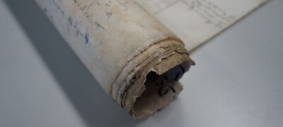 A close-up of the edges of a rolled parchment document, which are torn and damaged.