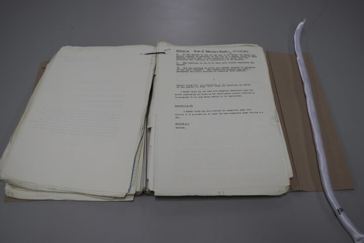 An open tagged file on a table. A white snake weight vertically weighs down the right side of the protective folder.