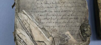 A stack of papers on a table. The lower left corners of the top pages are folded and torn, obscuring access to the written text.