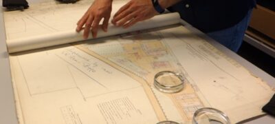 A large map is being unrolled on a table. Glass weights help to keep it flat as it's unrolled.