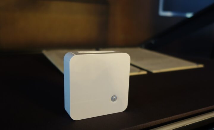 A square white box in a display case sits in front of two pages from a document.