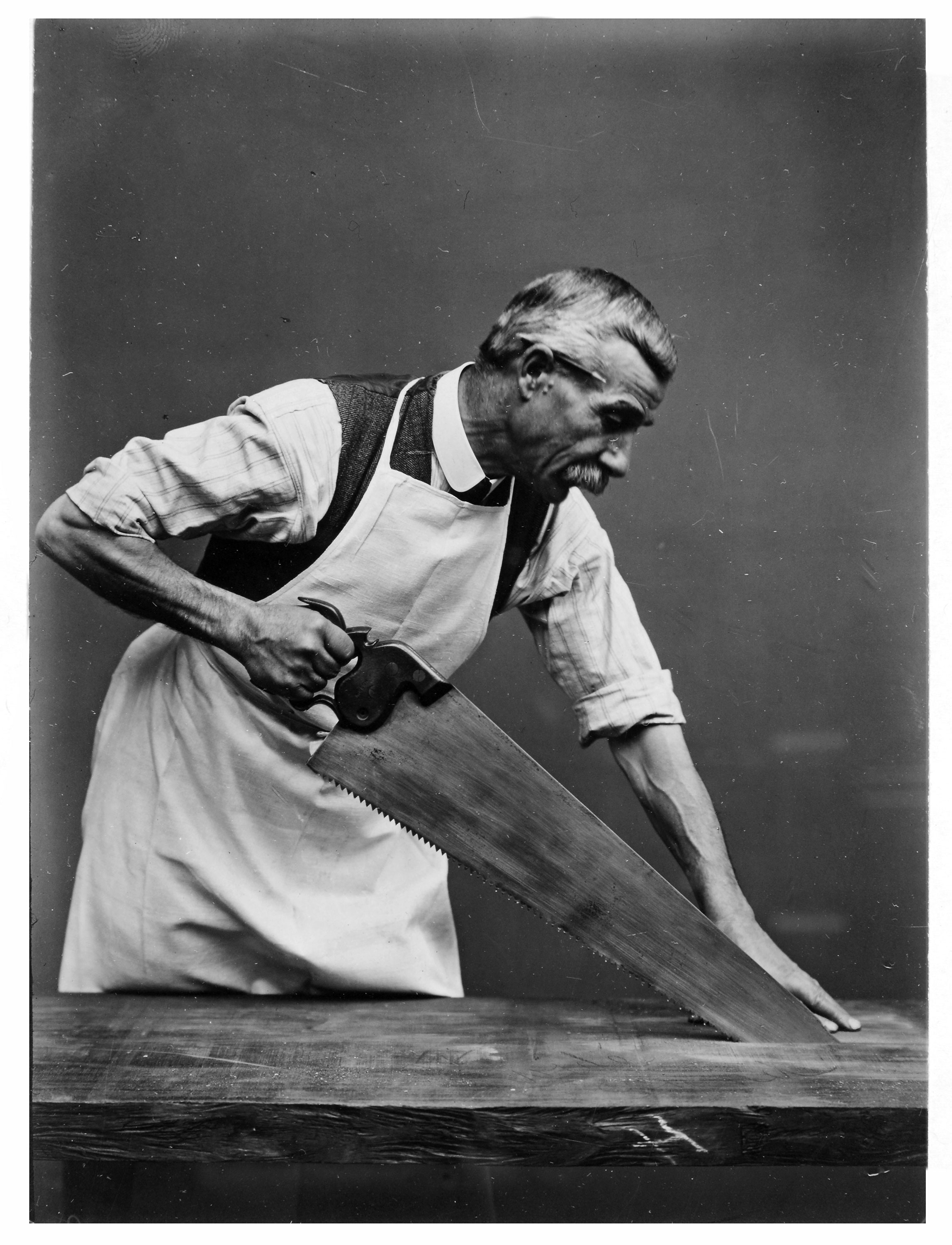 A photograph of a man using a handsaw to cut a piece of wood