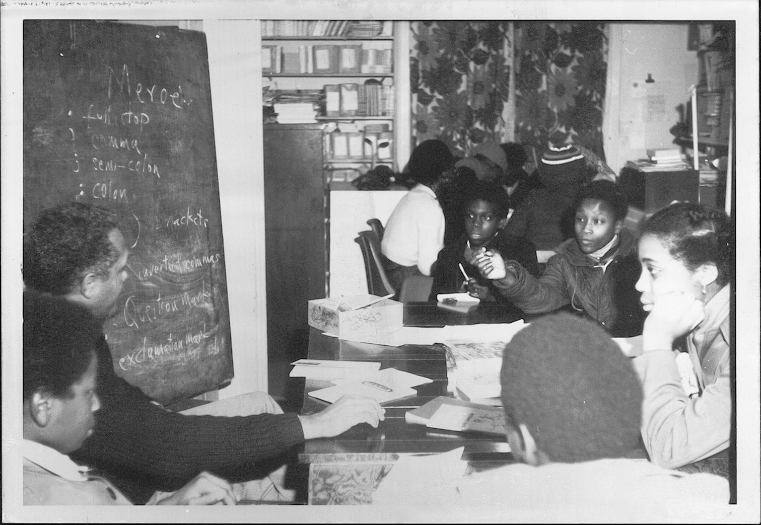 Students sat at tables near a teacher with a blackboard