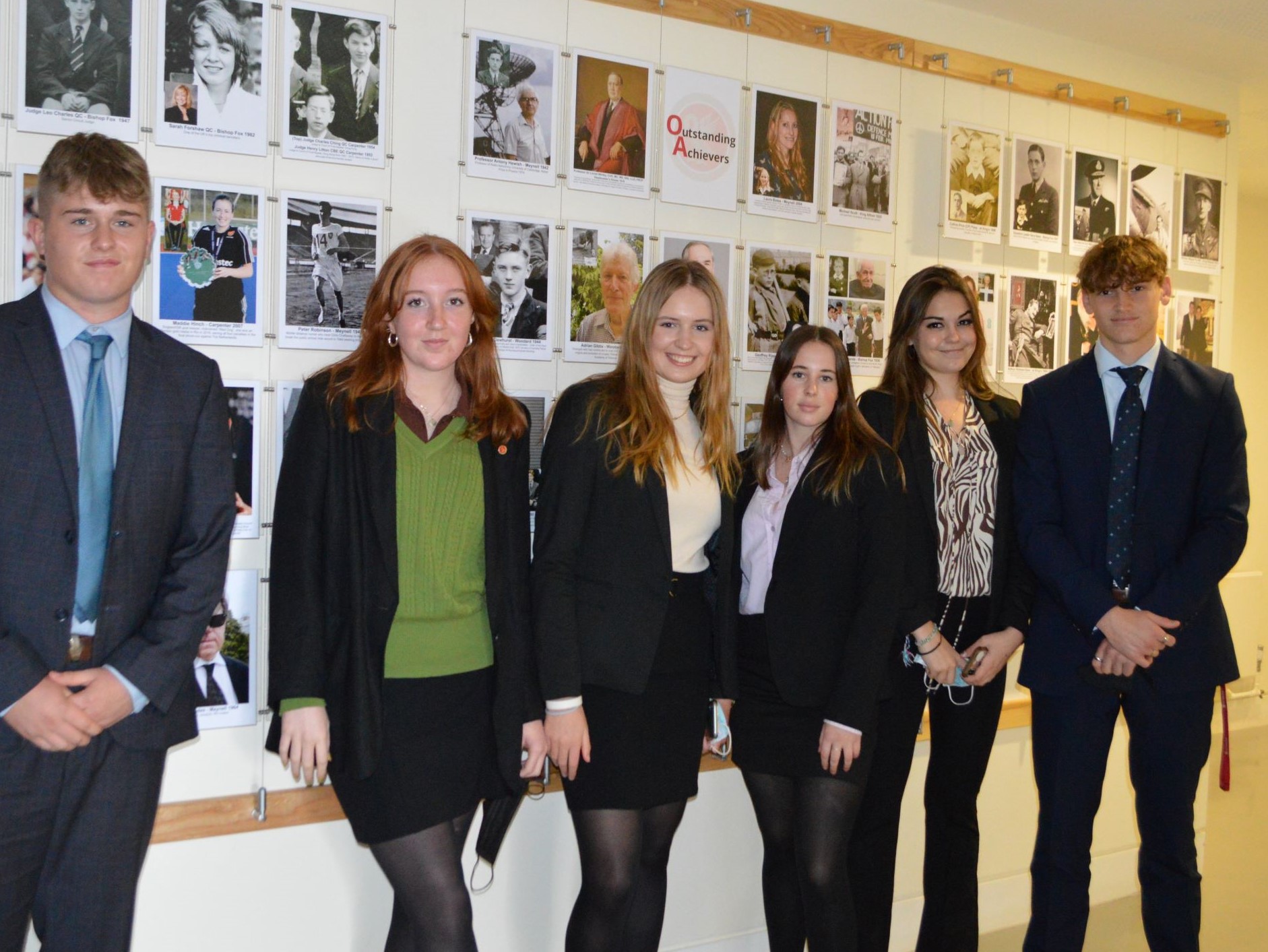 A row of students stand in front of a display of the school's alumni