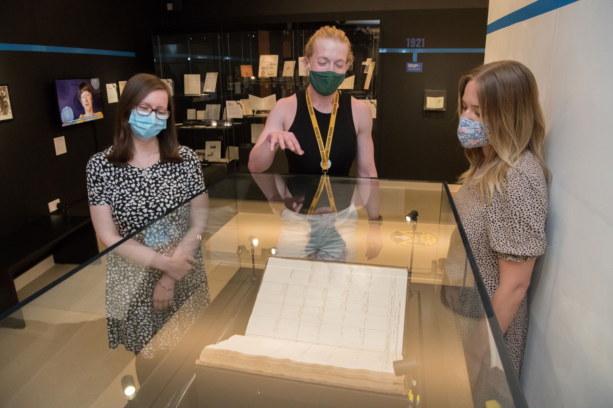 Three people gathered round a large book in a glass exhibition case