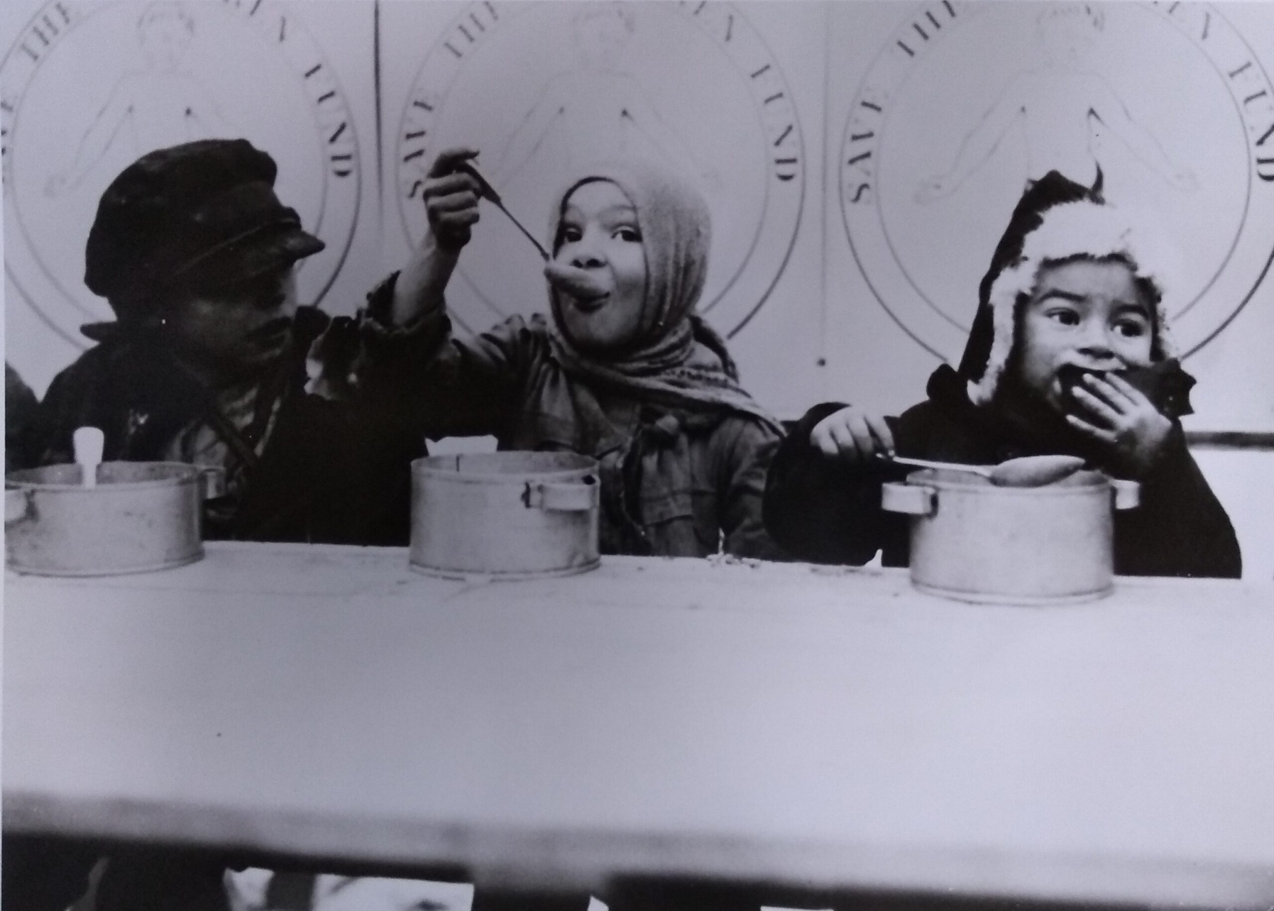 Three children in winter clothing eating from bowls