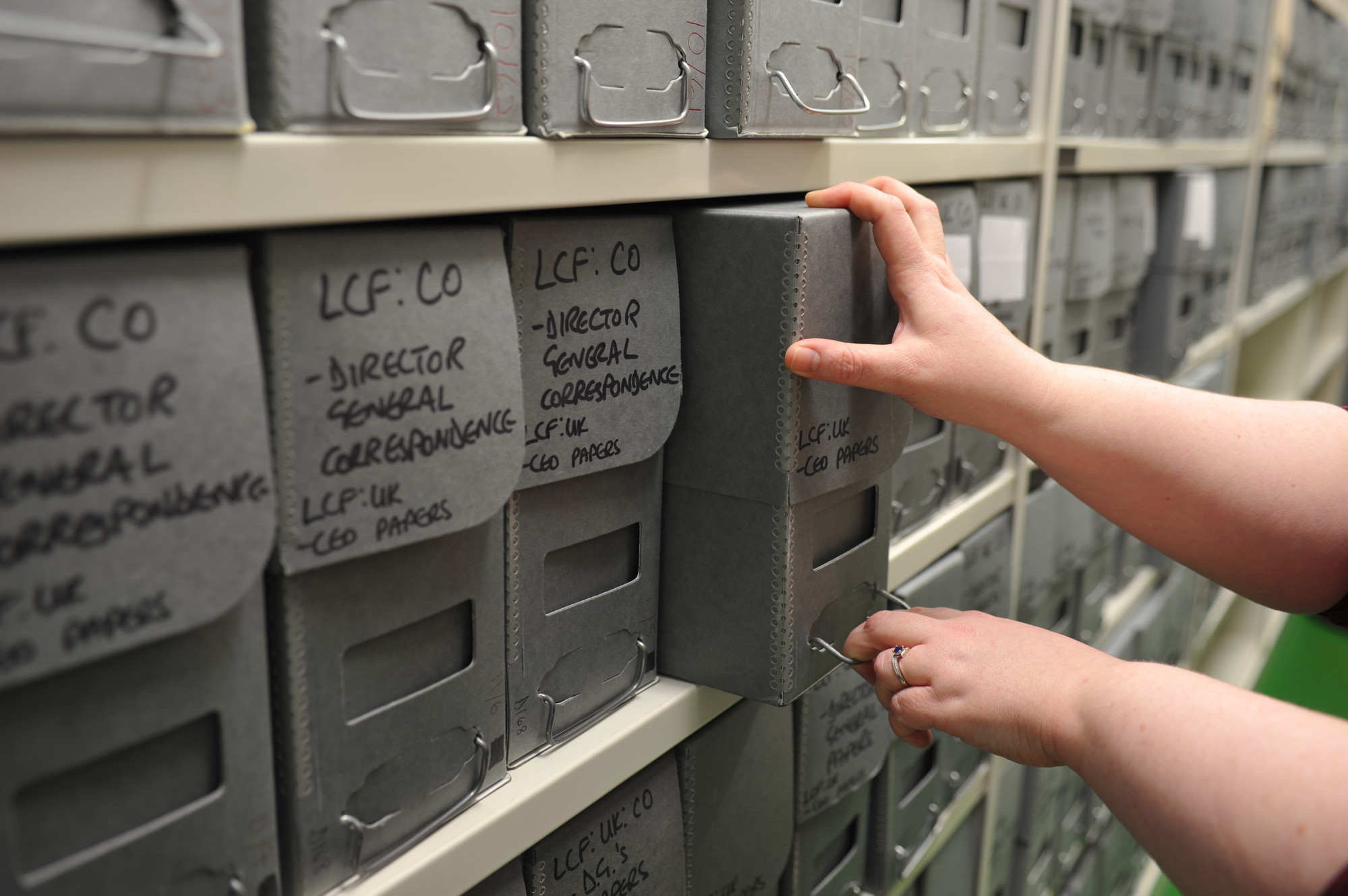 Two hands reaching and pulling a grey archive box off a shelf