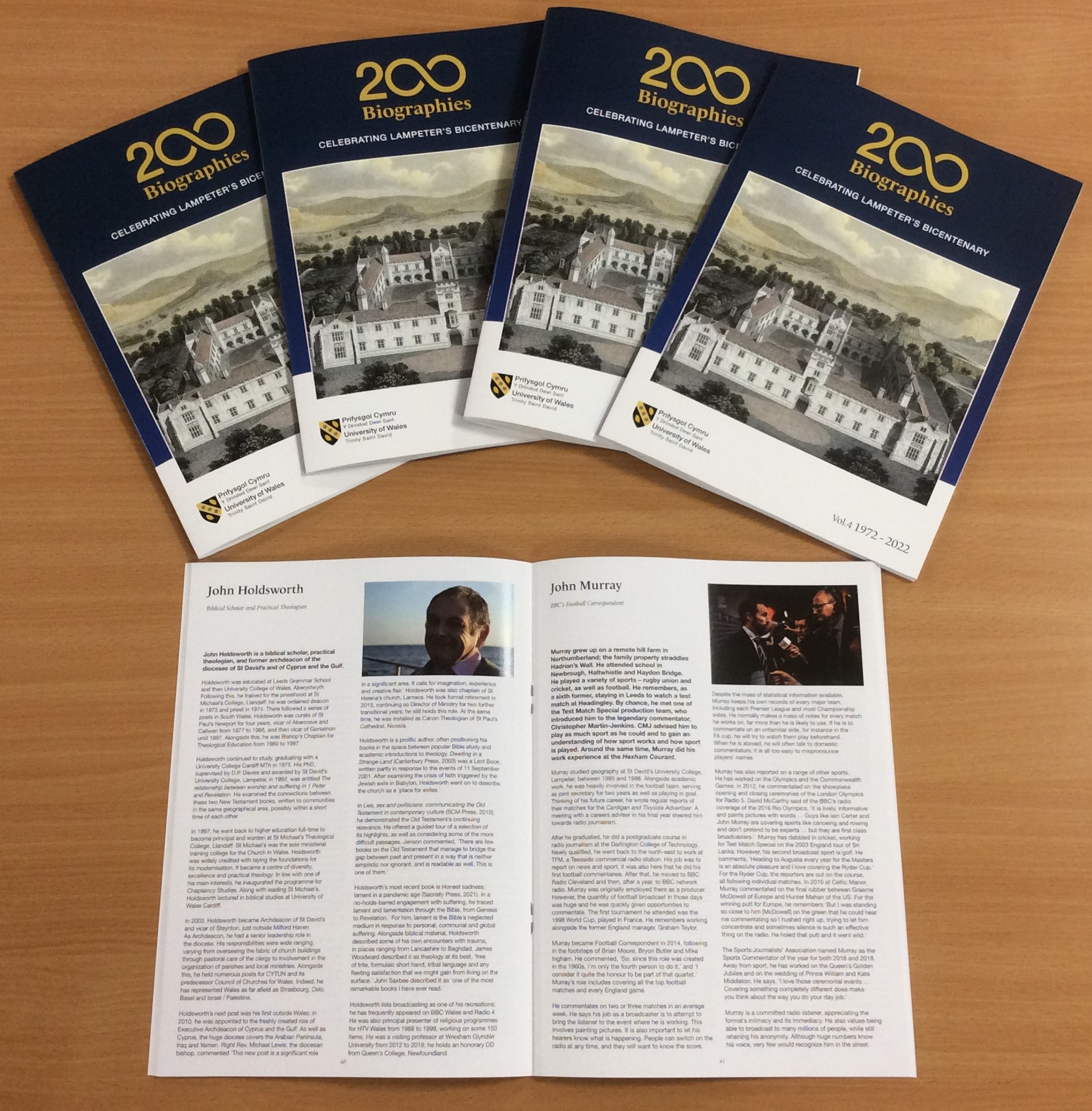 Five copies of the 200 biographies brochure laid on a table with one copy open