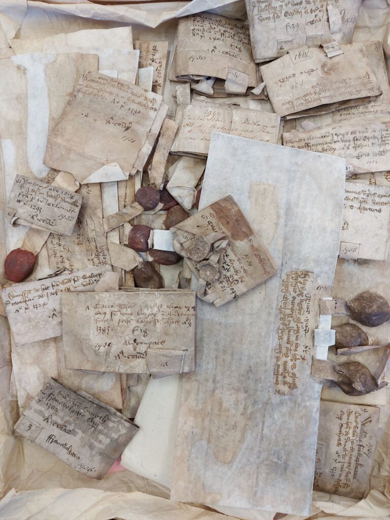 A series of medieval deeds - folded handwritten documents with red or brown wax seals attached - grouped together in a loose pile