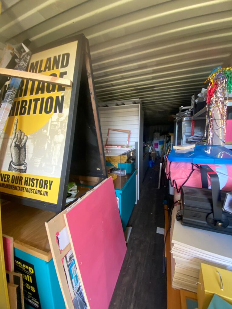 A dark, windowless storeroom containing a variety of materials, posters, and other items