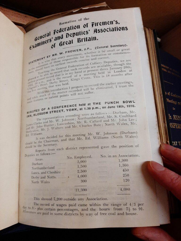 A hand holding a book open at a page titled 'Formation of the General Federation of Firemen's, Examiners' and Deputies' Associates of Great Britain'