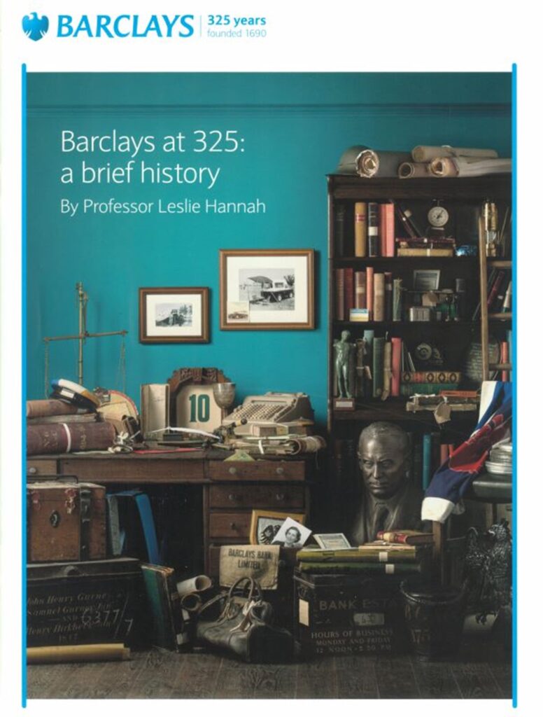 An A4 page layout with a special version of Barclays' blue-on-white at the top, with '325 years - founded 1690' to the right of it. The rest of the A4 page is taken up by an image of a teal-painted room that contains an antique wooden desk and bookcase, and a host of antique items such as a pair of scales, a brass bust of a man, some books and some parchment rolls. In the top left of the image is some white text, which reads 'Barclays at 325: A brief history, By Professor Leslie Hannah'