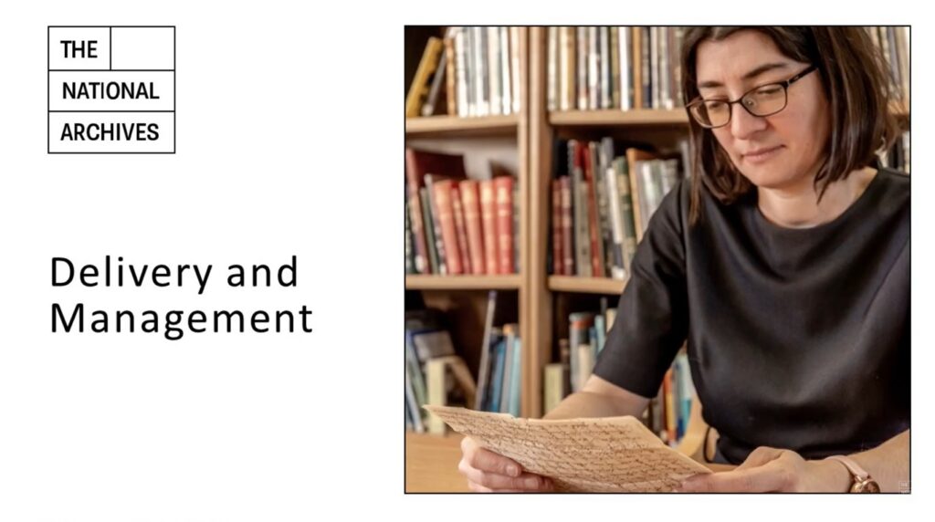White presentation slide, with 'Delivery and Management' typed in black on the left of the page, halfway down. The National Archives logo is top left. On the right, just over half of the slide is taken up with an image of a person with dark hair, cropped just above their shoulders, sitting at a wooden table. They are wearing a black short-sleeved garment, and holding a page of handwritten parchment
