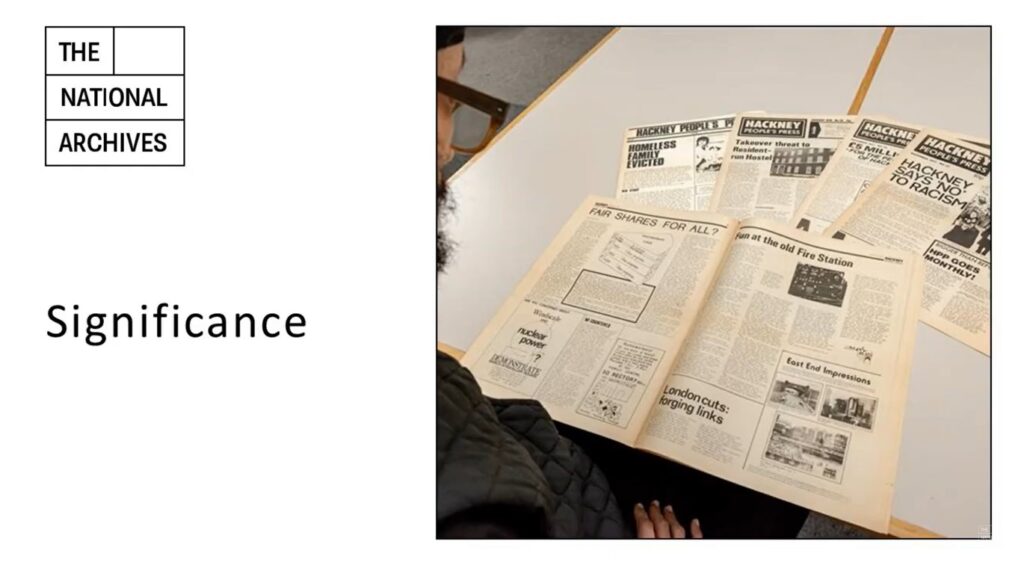 A person with a dark beard, wearing glasses and dressed in black, reading an archived edition of 'Hackney People's Press'. Four additional copies of different editions are also on the table, in a fan-shaped display