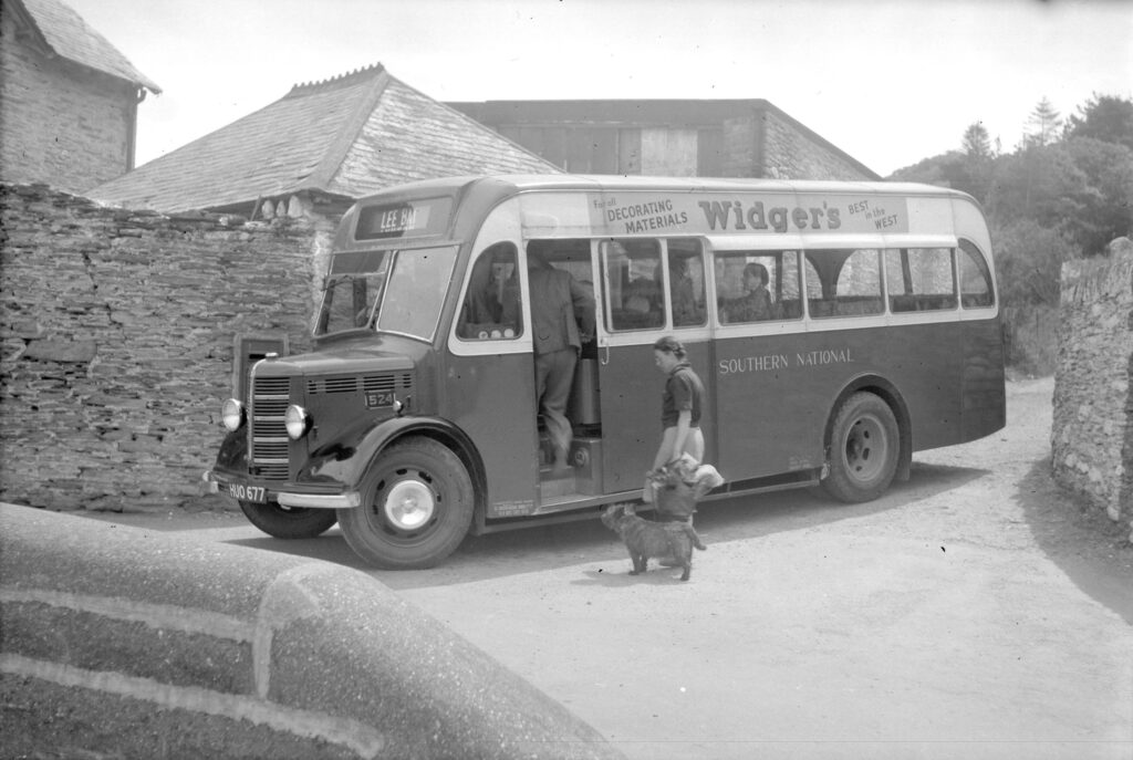 A woman and her dog waiting to board a small Southern National bus