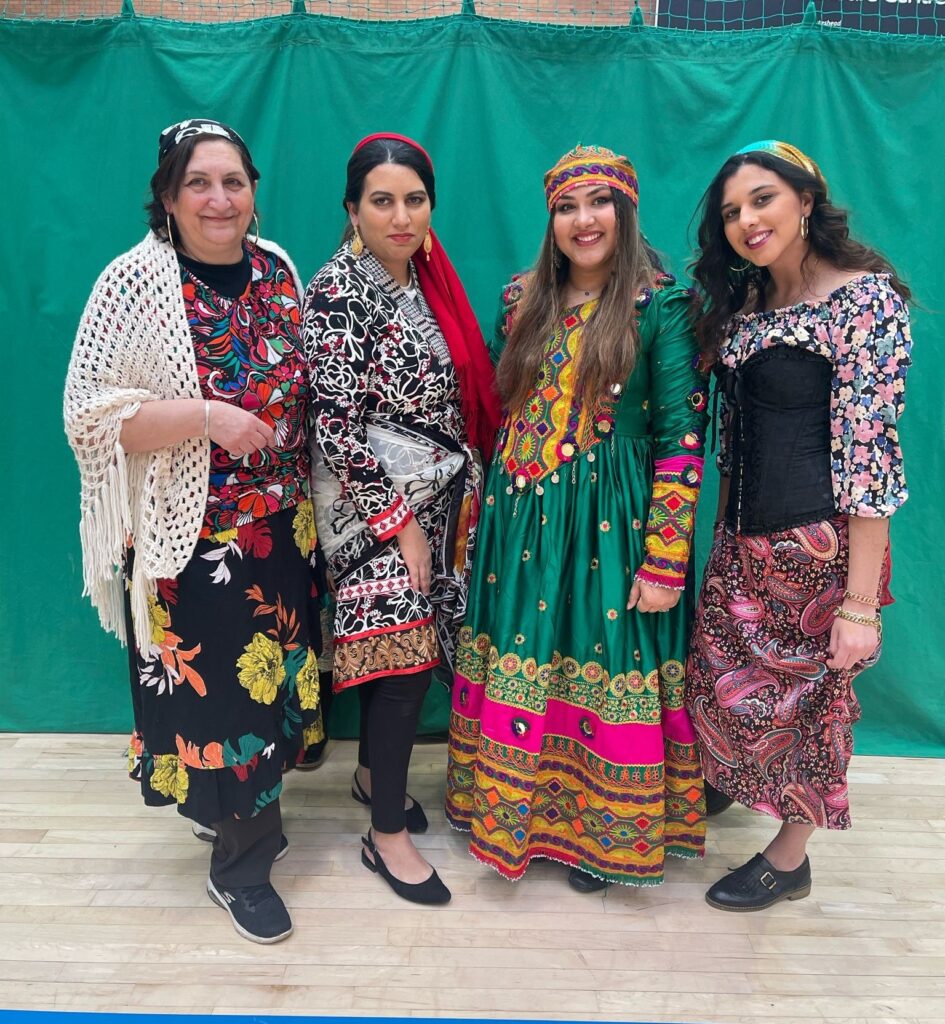 Four women pose for the camera wearing colourful patterned dresses.