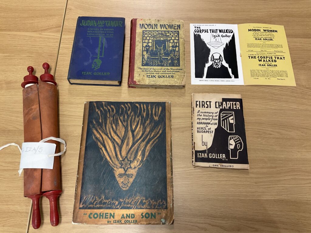 Several documents laid out on a wooden surface. These include old books, an open leaflet and a rolled up scroll.