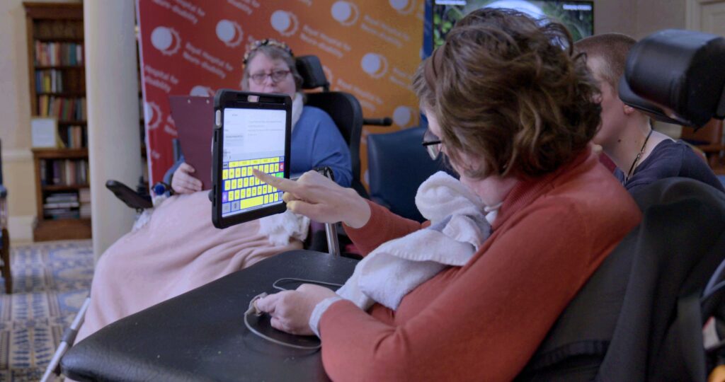 A person sat in a wheelchair and typing on a keyboard that is displayed on the screen attached to the chair