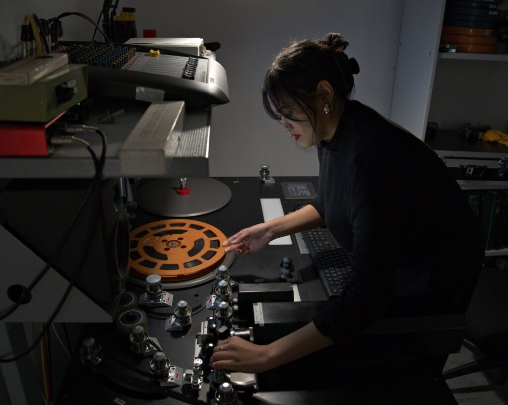 A woman in a dark studio uses audio-visual equipment on an old film reel.