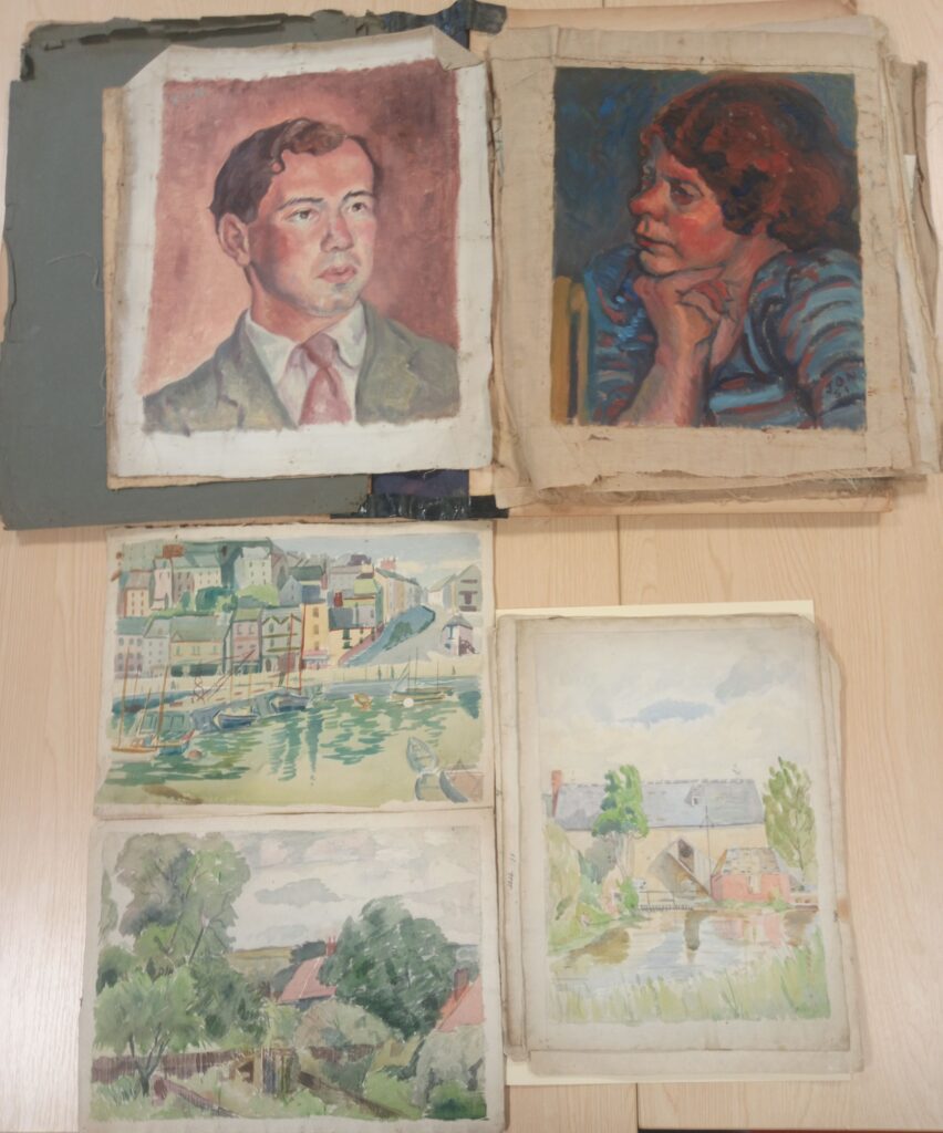 A selection of hand paintings laid out on a wooden table. Two of the paintings are respective portraits of a man and a woman. The other three are exterior shots showing a harbour, trees and a house on a river.