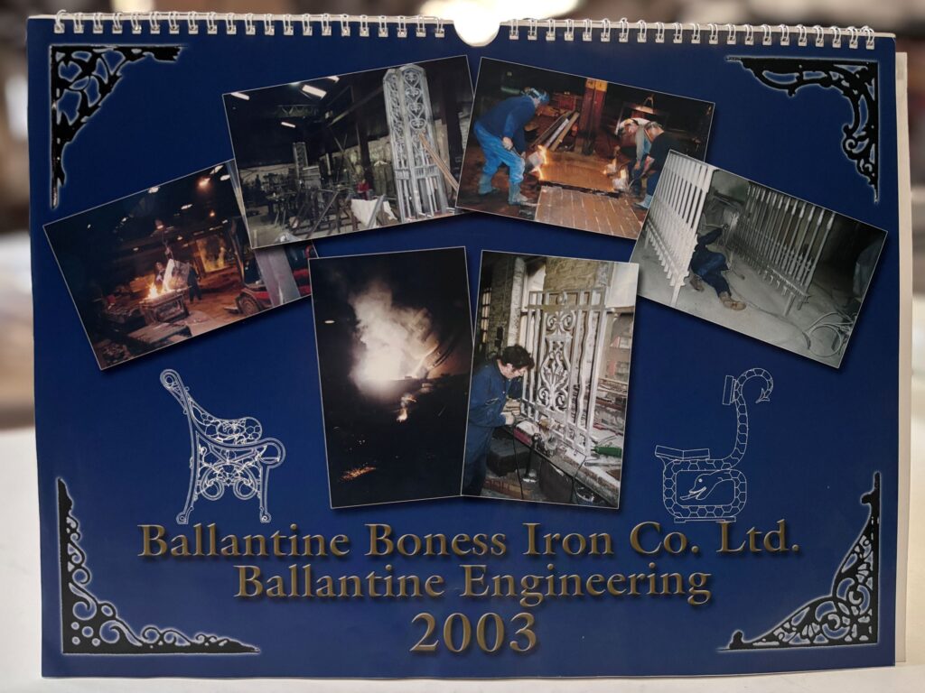 Close-up of a dark blue calendar cover showing several images of iron workers building rails and structures. Golden text at the bottom reads: 'Ballantine Bones Iron Co. Ltd. Ballantine Engineering 2003'.