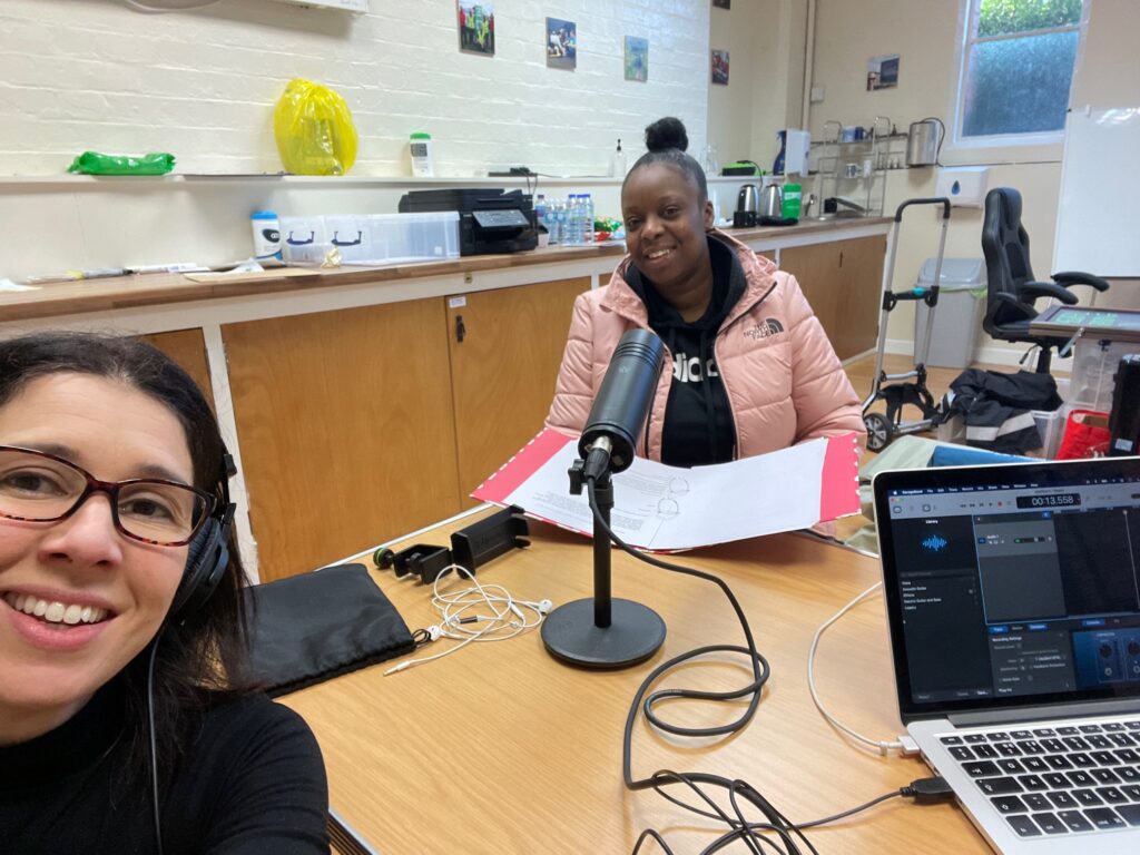 Two people sat at a table with a laptop and a microphone, recording a podcast