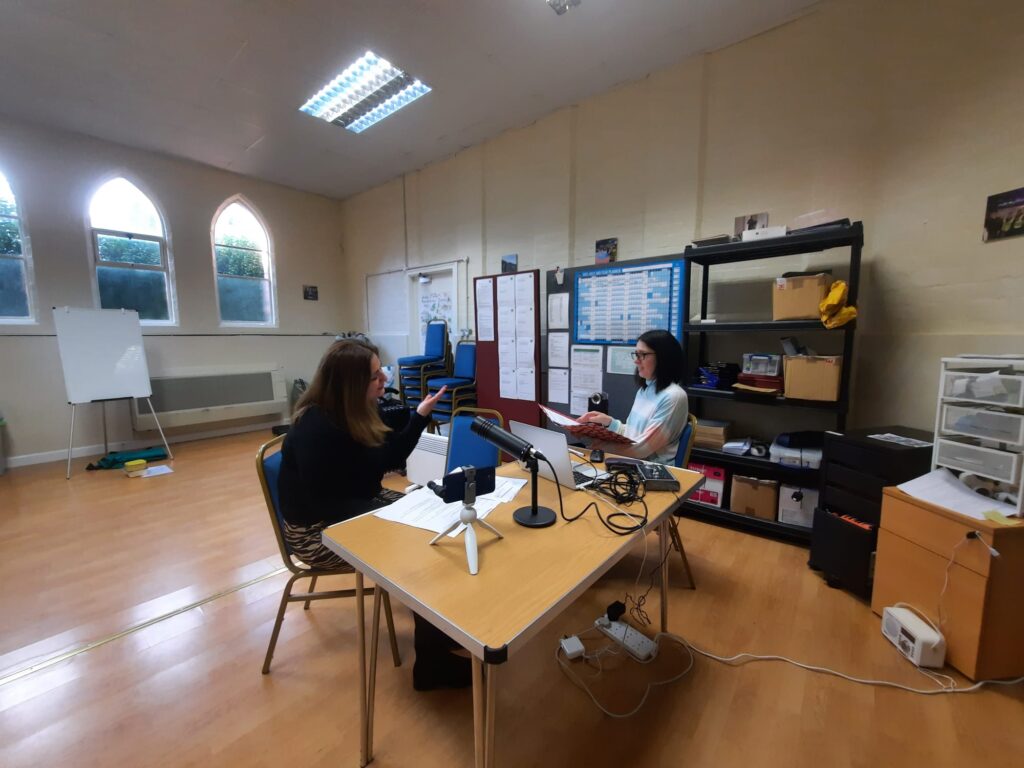 Two people at a table recording a podcast in a room