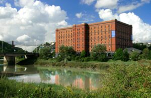 A wide shot of Bristol Archives - a red brick building stood next to a river and beside a large concrete bridge.
