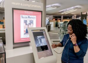 A woman interacts with a display screen, listening to information through a heavy duty handset.