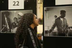 A young woman looks at an exhibition of black and white photographs of musicians from the 1980s.