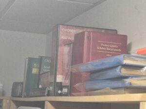 A shelf of files and record books in the top corner of a room. The most prominent is red, leather bound and is entitled 'Product Liability & Safety Encyclopaedia'