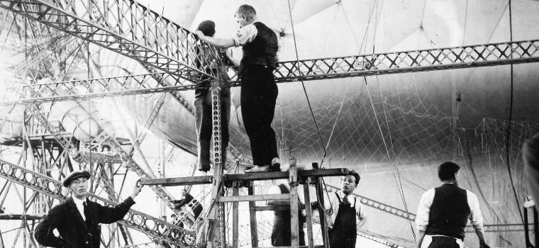 A black and white photograph from the 1920s in which we see architects at work as a construction takes shape.