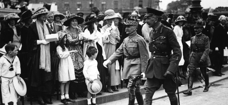 Senior army officials are shown walking through the streets in front an applauding crowd. Here we see well-dressed women and children.