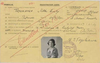 Hilda Toyokawa's alien registration card, recording her return to the UK from America as an 'alien'. The card features a black and white photo of Hilda in the middle bottom of the card, which is printed on yellow card, in landscape format. 'Cancelled' is written across the card in red handwriting, marking the moment she regained her British nationality.