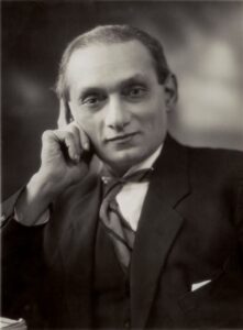 Black and white portrait of Shapurji Saklatvala, taken in 1922. Shapurji is looking at the camera, his right hand resting against his head. His is wearing a suit and tie.