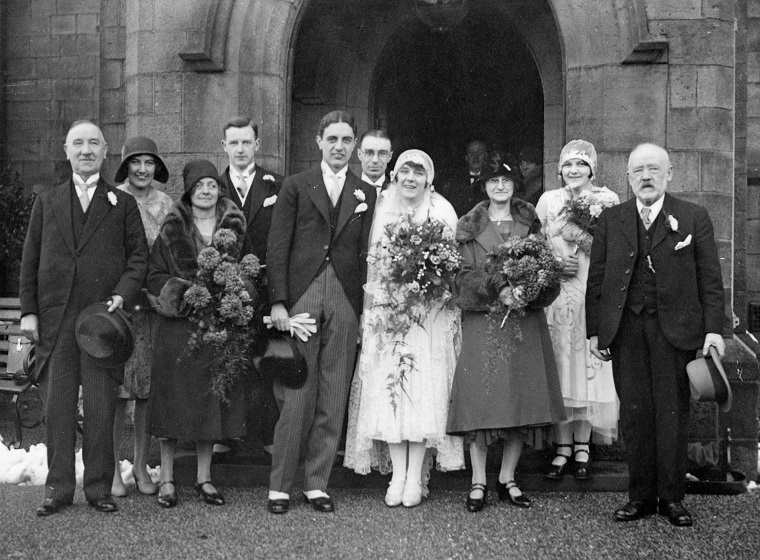 A black and white wedding photo with bride, groom and family standing outside the entrance of a church. Taken in 1929.