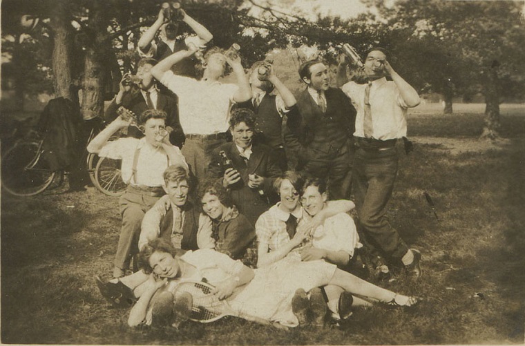 Black and white photo of 11 friends, posing with empty bottles in a park, 1923.
