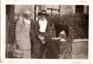 Two women stand outside a house, next to a pram with an infant in it. c.1922.