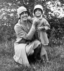 A woman standing in a field with her young daughter, c. 1928. She is holding a buttercup under her daughter's chin.