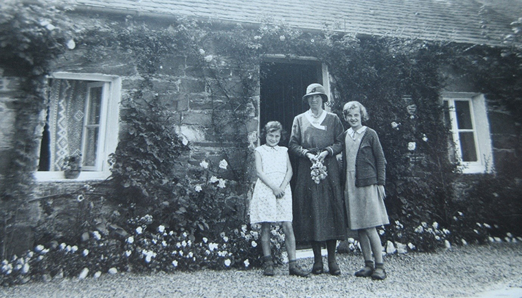 A mother stands in between her two daughters, outside a cottage in Port-na-Craig, Perthshire.