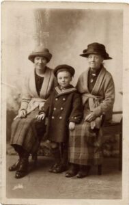 A mother and grandmother sit on a bench, with their (grand)son standing in between them.