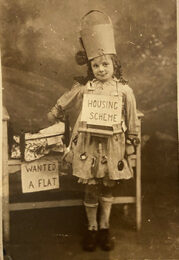 An eight year old girl in fancy dress, wearing a 'housing scheme' sign, purportedly relating to the Housing Bill of 1921.