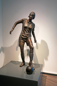 Bronze statue of Lily Parr playing football with the ball at her feet.