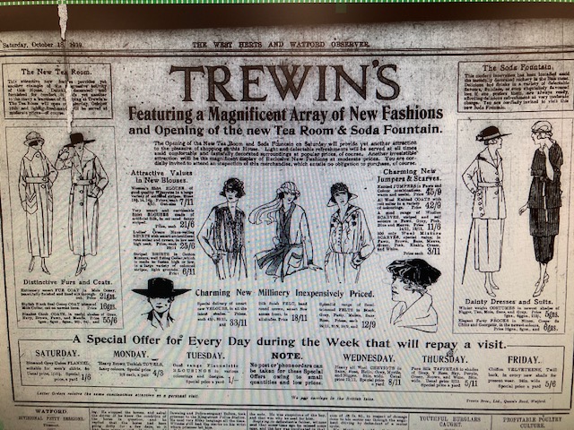 A newspaper clipping dated October 1919 from the West Herts and Watford Observer showing an advert for Trewin's featuring 'A magnificent array of new fashions' and 'opening of the new tea room and sofa fountain'. Drawings of 1920s fashions including 'distinctive furs and coats' on the letf hand side, new blouses, jumpers, scarves and millinnery in the middle section and 'dainty dresses and suits' on the right hand side. 