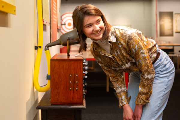 An image of a girl with her head to a speaker attached to a pipe listening to sound